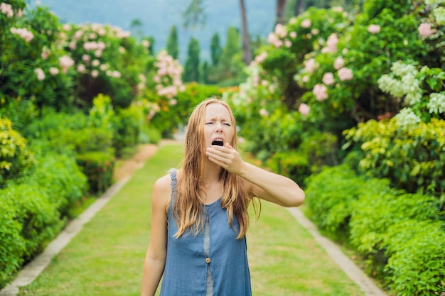 La giovane donna starnutisce nel parco sullo sfondo di un albero in fiore. Allergia al concetto di polline