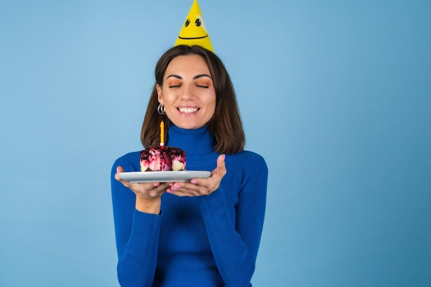 La giovane donna su un muro blu festeggia un compleanno, tiene in mano un pezzo di torta, di ottimo umore, felice, eccitata