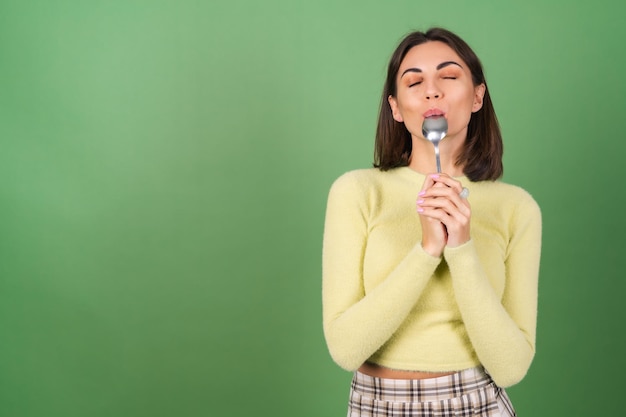 La giovane donna sul verde in un maglione giallo con appetito mangia da un cucchiaio, godendo