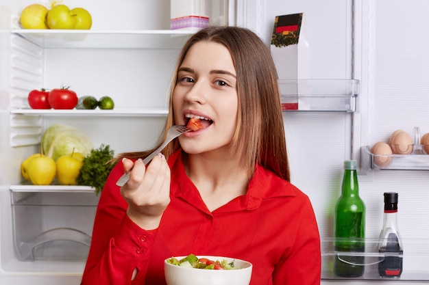 La giovane donna sveglia assaggia l'insalata vegetariana fresca deliziosa