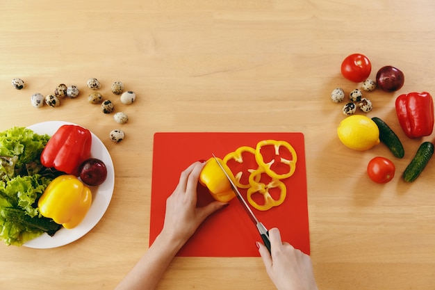 La giovane donna taglia il peperone giallo per insalata con un coltello in cucina. Concetto di dieta. Uno stile di vita sano. Cucinare a casa. Prepara da mangiare. Vista dall'alto.