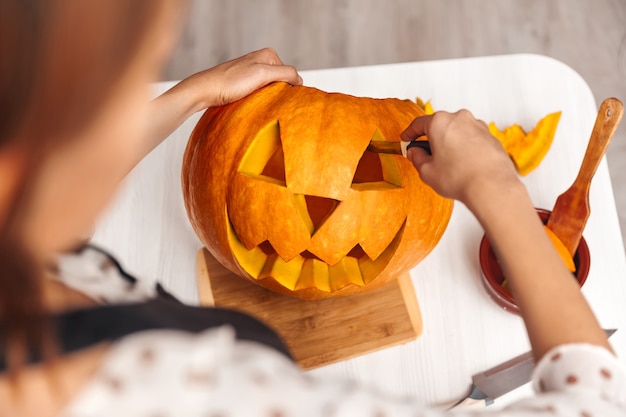 La giovane donna taglia una zucca per Halloween al chiuso, vista dall'alto