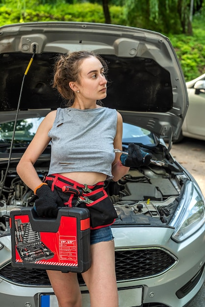 La giovane donna tiene gli strumenti per la riparazione e in attesa di aiuto vicino all'auto rotta