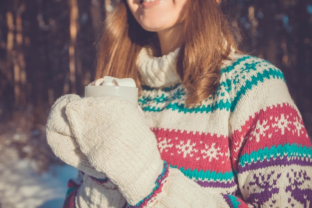 La giovane donna tiene una tazza di caffè con marshmallow nella foresta invernale