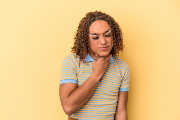 La giovane donna transessuale latina isolata su sfondo giallo soffre di dolore alla gola a causa di un virus o di un'infezione.