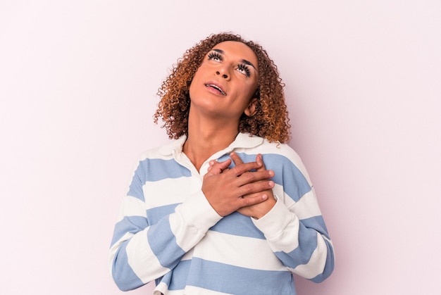 La giovane donna transessuale latina isolata su sfondo rosa ha un'espressione amichevole, premendo il palmo sul petto. Concetto di amore.