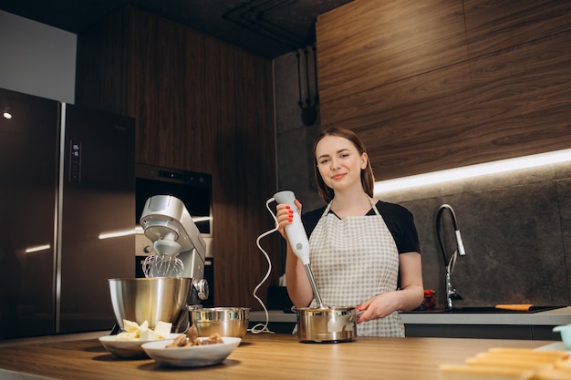 La giovane donna usa il mixer e monta la panna per i supporti per dolci nella cucina moderna