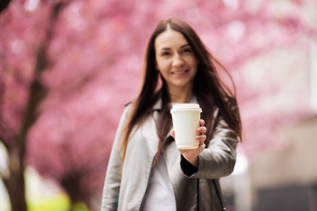 La giovane e bella donna con lunghi capelli scuri gode della bellezza della natura primaverile vicino all'albero di fioritura di sakura