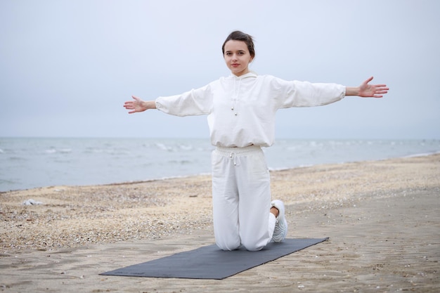 La giovane e bella ragazza seduta sul tappetino da yoga e ha aperto le braccia spalancate Foto di alta qualità