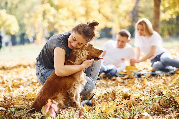 La giovane famiglia allegra con il cane si riposa insieme in un parco autunnale.