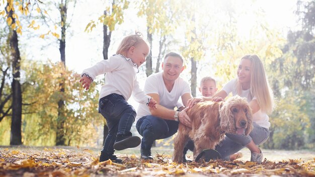 La giovane famiglia allegra con il cane si riposa insieme in un parco autunnale.