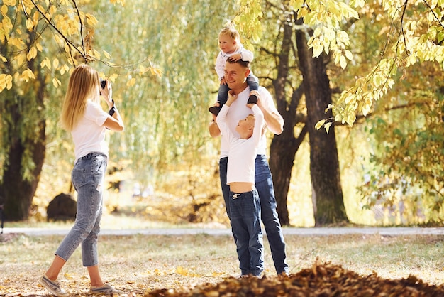 La giovane famiglia allegra fa una passeggiata insieme in un parco autunnale.