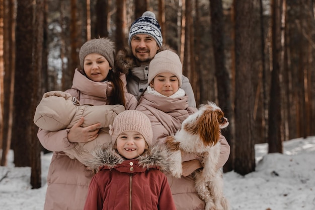 La giovane famiglia caucasica felice gioca con un cane in inverno in una foresta di pini