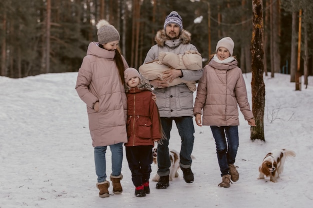 La giovane famiglia caucasica felice gioca con un cane in inverno in una foresta di pini