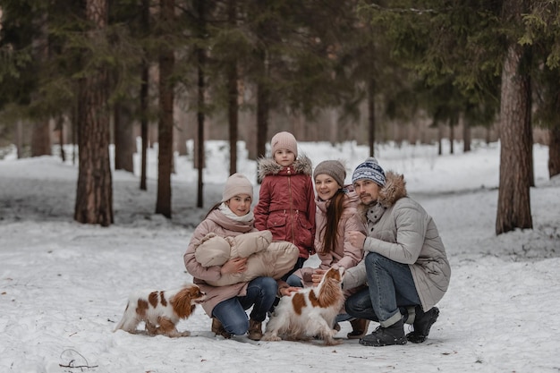 La giovane famiglia caucasica felice gioca con un cane in inverno in una foresta di pini