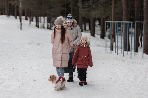 La giovane famiglia caucasica felice gioca con un cane in inverno in una foresta di pini