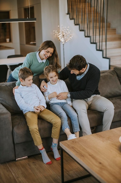 La giovane famiglia felice con due bambini si diverte insieme sul divano nel soggiorno