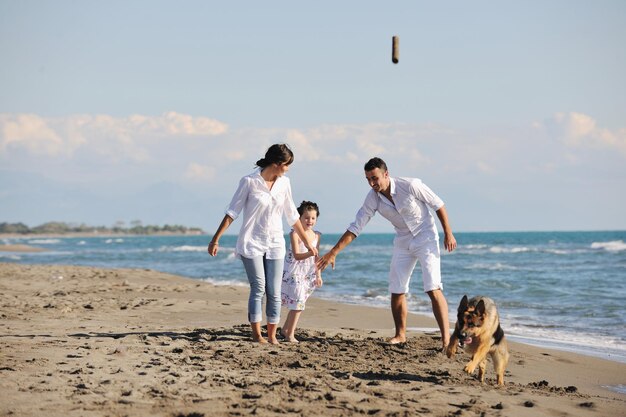 la giovane famiglia felice in abiti bianchi si diverte e gioca con un bel cane in vacanza sulla bellissima spiaggia