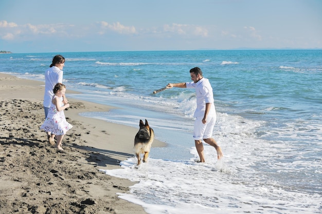 la giovane famiglia felice in abiti bianchi si diverte e gioca con un bel cane in vacanza sulla bellissima spiaggia