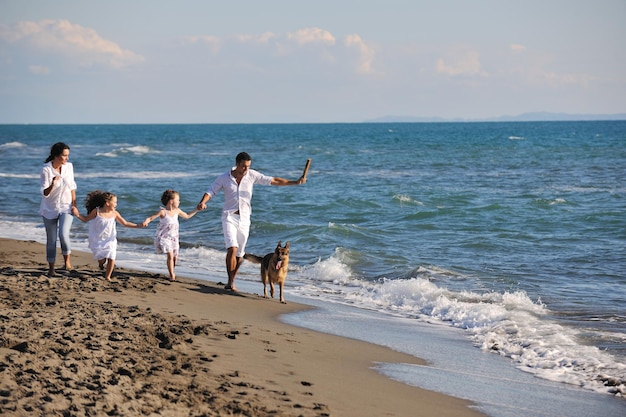 la giovane famiglia felice in abiti bianchi si diverte e gioca con un bel cane in vacanza sulla bellissima spiaggia