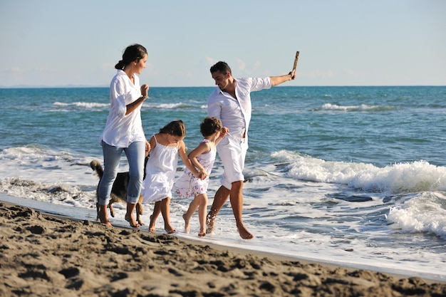 la giovane famiglia felice in abiti bianchi si diverte e gioca con un bel cane in vacanza sulla bellissima spiaggia