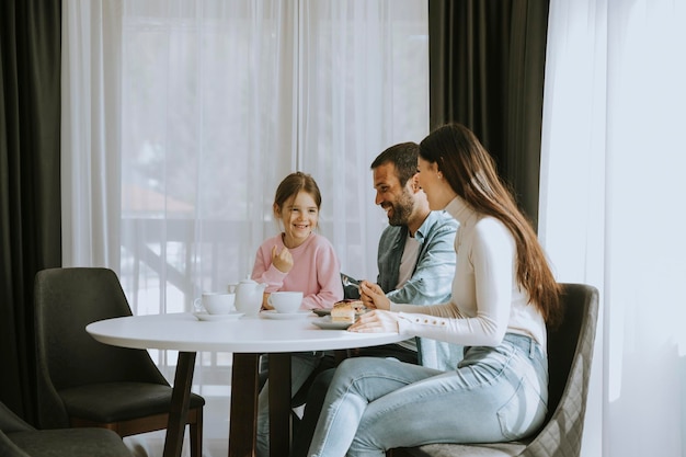 La giovane famiglia felice mangia dolci e beve il tè insieme nella stanza