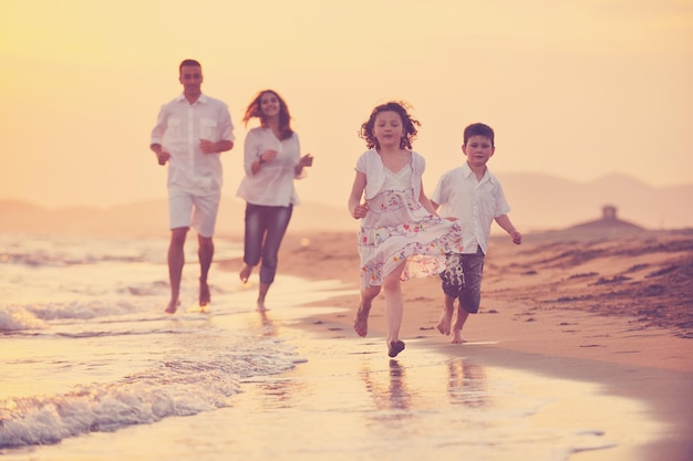 la giovane famiglia felice si diverte sulla spiaggia correre e saltare al tramonto