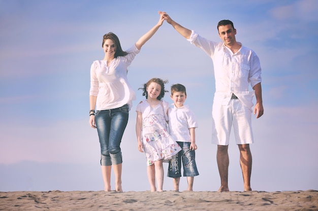 la giovane famiglia felice si diverte sulla spiaggia e mostra il segno di casa con le mani unite proteggendo i bambini