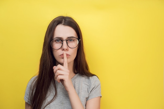 La giovane femmina con l'espressione scioccata dimostra il gesto di silenzio