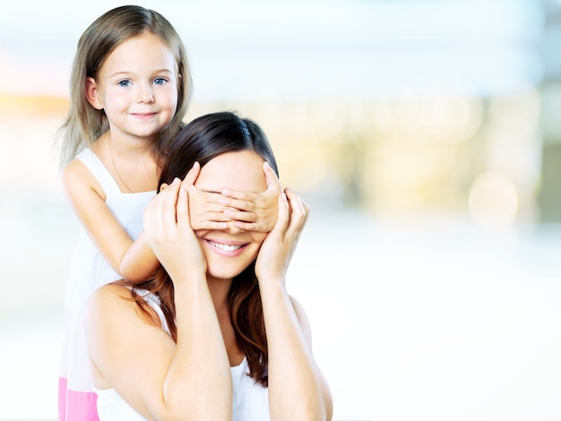 La giovane figlia chiude la mamma degli occhi delle mani - isolata. Concetto di famiglia felice.