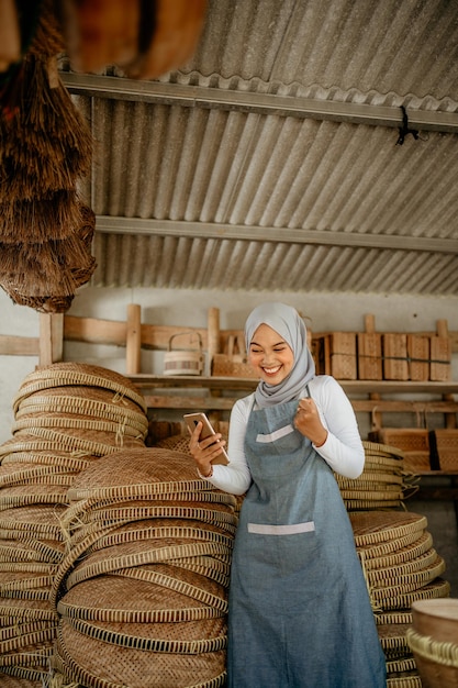 La giovane imprenditrice musulmana eccitata alza il braccio mentre usa il suo telefono cellulare