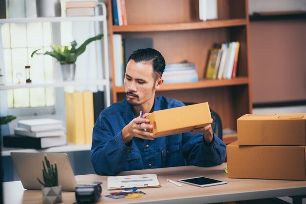 La giovane impresa avvia il proprietario del venditore online usando il portatile per controllare gli ordini dei clienti e preparare i pacchetti per il prodotto