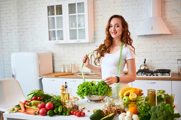 La giovane lattuga felice della tenuta della donna lascia per produrre l'insalata nella bella cucina con gli ingredienti freschi verdi all'interno. Cibo sano e concetto di dieta. Perdere peso