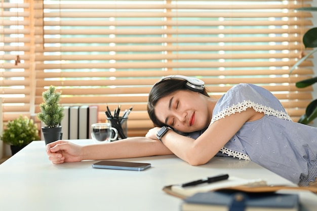 La giovane libera professionista che indossa le cuffie si addormenta distratta dal lavoro dormendo alla scrivania