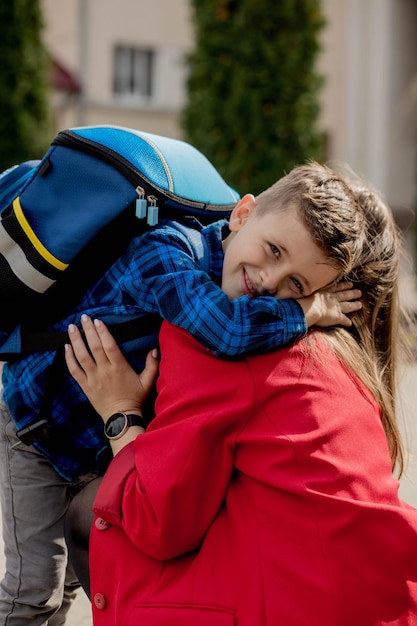 La giovane madre abbraccia il suo eccitato figlio di prima classe mentre va a scuola pronto a studiare