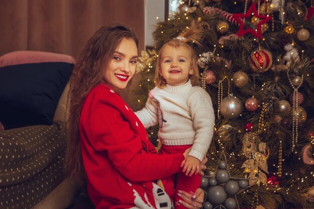 La giovane madre allegra abbraccia la sua piccola neonata all'albero di natale