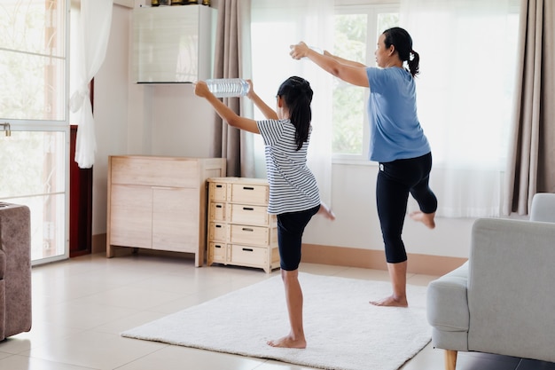La giovane madre asiatica e sua figlia fanno esercizio di stretching fitness yoga e usano la bottiglia d'acqua per essere manubri insieme a casa nella routine quotidiana.