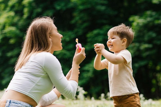 La giovane madre caucasica e il suo piccolo figlio felice si divertono a giocare con le bolle di sapone nel parco