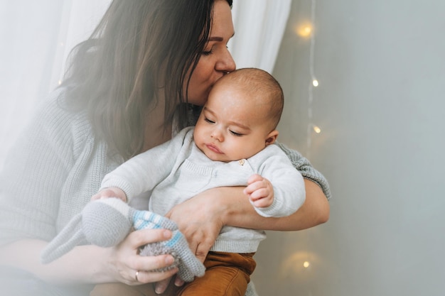 La giovane madre che gioca con il neonato sveglio nei toni naturali della camera da letto luminosa ama l'emozione