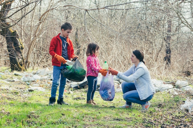 La giovane madre di famiglia con due bambini volontari pulisce il parco primaverile raccogliendo spazzatura e bottiglie di plastica