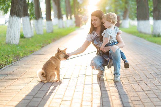 La giovane madre e il bambino giocano con un cane sull'erba. Cucciolo di shiba inu che gioca con la famiglia felice