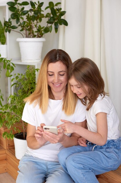 La giovane madre e la figlia usano lo smartphone e sorridono mentre si siedono sul divano di casa