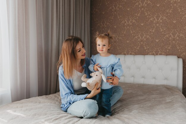 La giovane madre felice gioca con sua figlia sul letto a casa. festa della mamma.