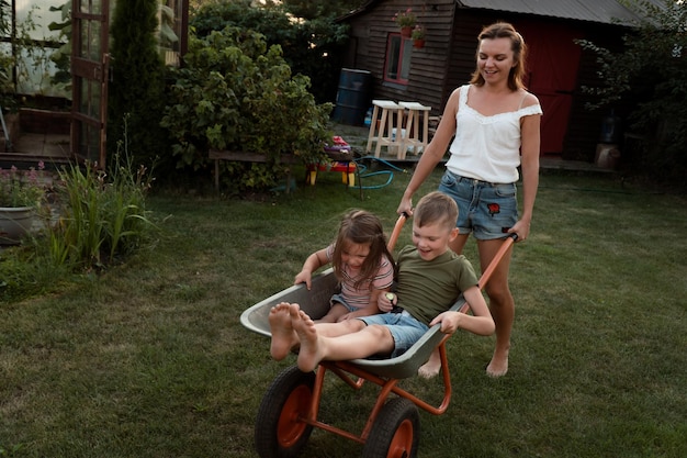 La giovane madre gioca con i bambini e il carrello da giardino al dackyard