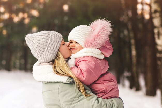 La giovane madre in inverno tiene la sua piccola figlia tra le braccia e la bacia. Ritratto di famiglia. Maternità e infanzia