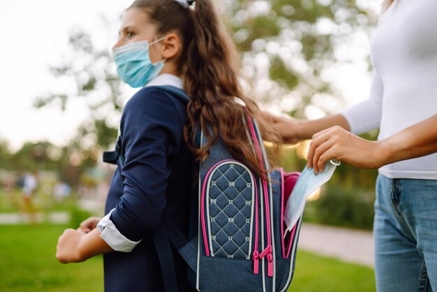 La giovane madre mette una maschera sterile protettiva nello zaino della scolaretta La vita durante la pandemia covid19