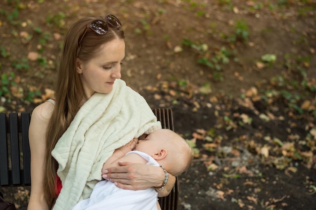 La giovane madre nutre il bambino su una panchina nel parco Mamma che allatta il bambino in un luogo pubblico