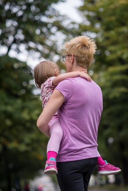 la giovane madre sportiva porta la piccola figlia in braccio mentre fa jogging in un parco cittadino, sport all'aria aperta e fitness
