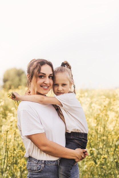 La giovane madre tiene sua figlia in estate su un campo fiorito. Bella famiglia e gioia della maternità.