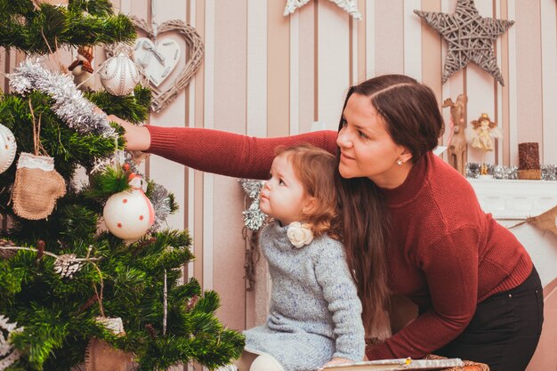 La giovane mamma aiuta la tua piccola figlia a decorare l'albero di Natale